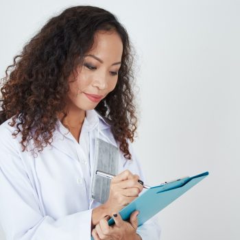 Asian young doctor standing and writing medical report on clipboard